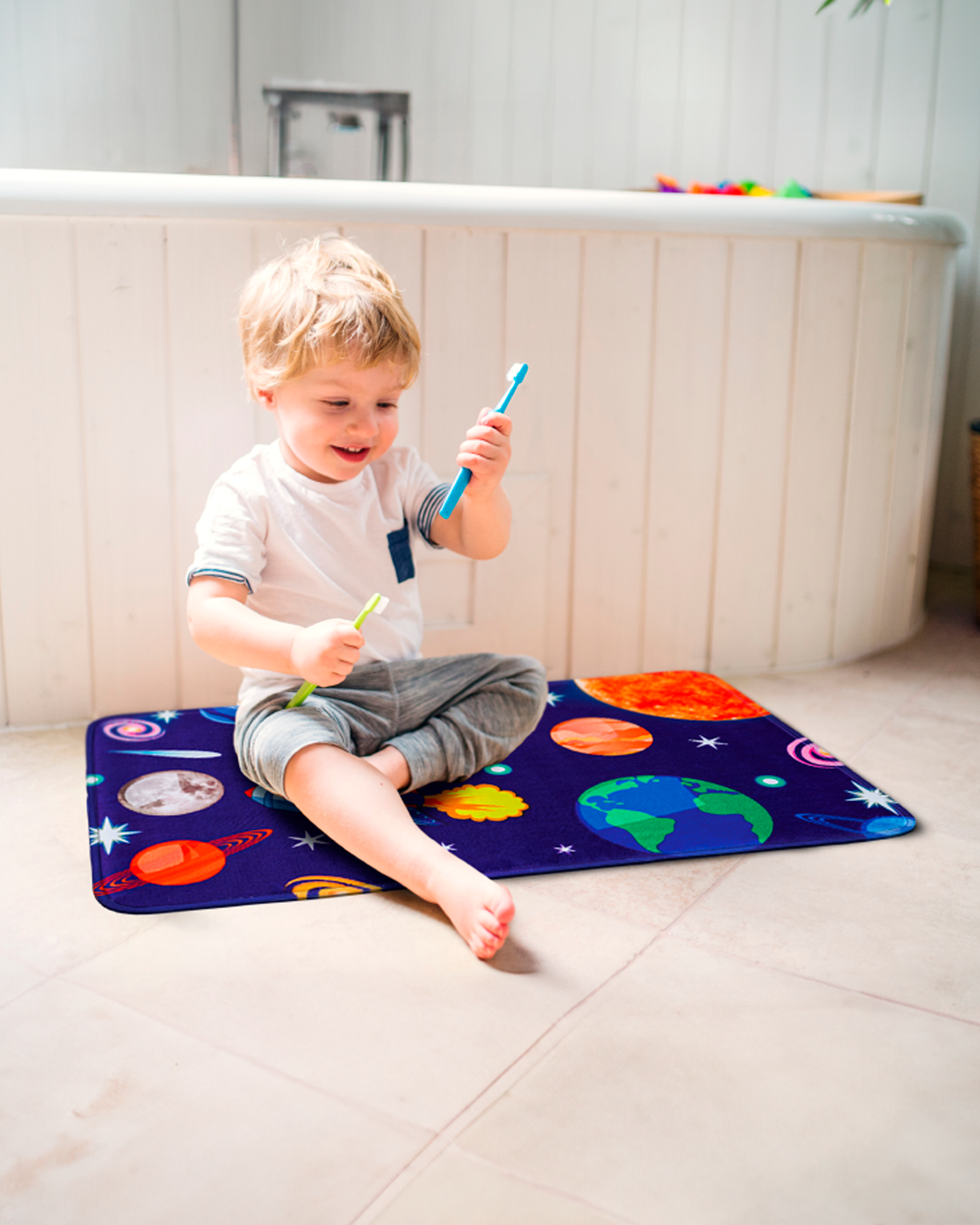 A happy toddler sitting on the Khelo Space-Themed Kids Bath Mat, enjoying a fun moment with toothbrushes. This vibrant and educational bath mat features astronauts, planets, and stars, adding a playful touch to any kids' bathroom. Made with ultra-soft, cushioned fabric and a non-slip backing, this bath rug ensures safety, comfort, and durability. Perfect for bath time, playtime, and everyday use in a space-themed kids' bathroom.