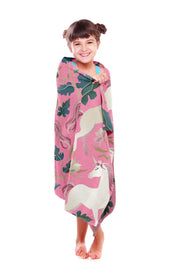 Smiling young girl wrapped in a pink unicorn organic cotton towel, showcasing a charming design with elegant white unicorns, lush floral patterns, and soft pastel tones. This ultra-soft and highly absorbent towel is made from 100% organic cotton, offering breathable comfort and quick-drying properties. Perfect for bath time, beach outings, and poolside fun, this premium-quality towel by Khelo ensures warmth and coziness with every use. Designed to be fade-resistant for up to 500 washes, it’s a long-lasting 